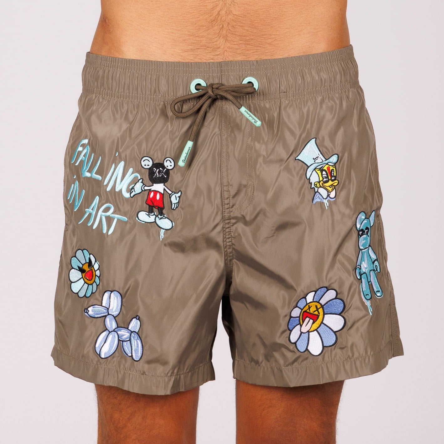 Khaki swim shorts front view with illustrated graphic and “Falling in art” text