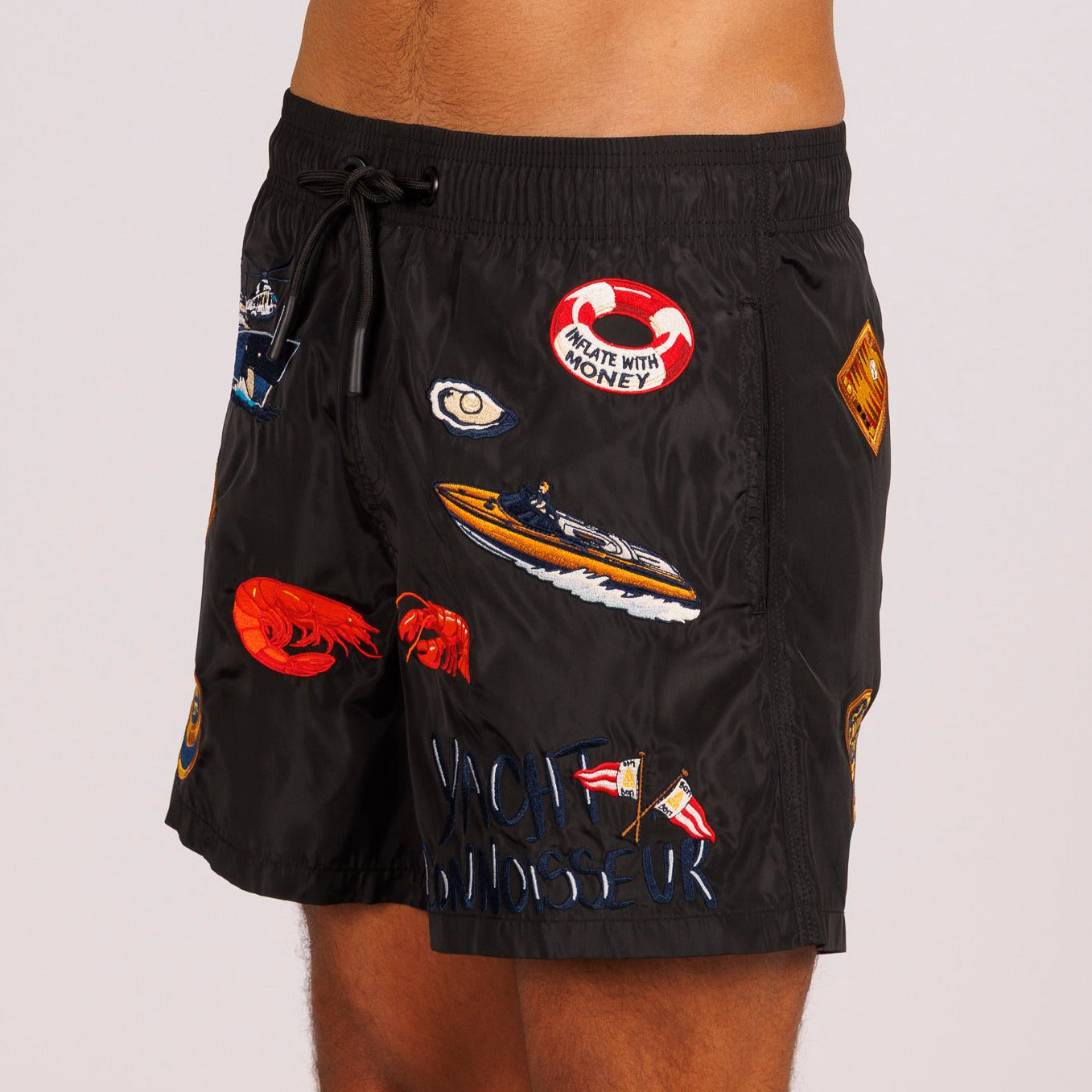 Black swim shorts side view with illustrated graphic and “Yacht connoisseur” text