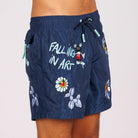 Navy blue swim shorts side view with illustrated graphic and “Falling in art” text