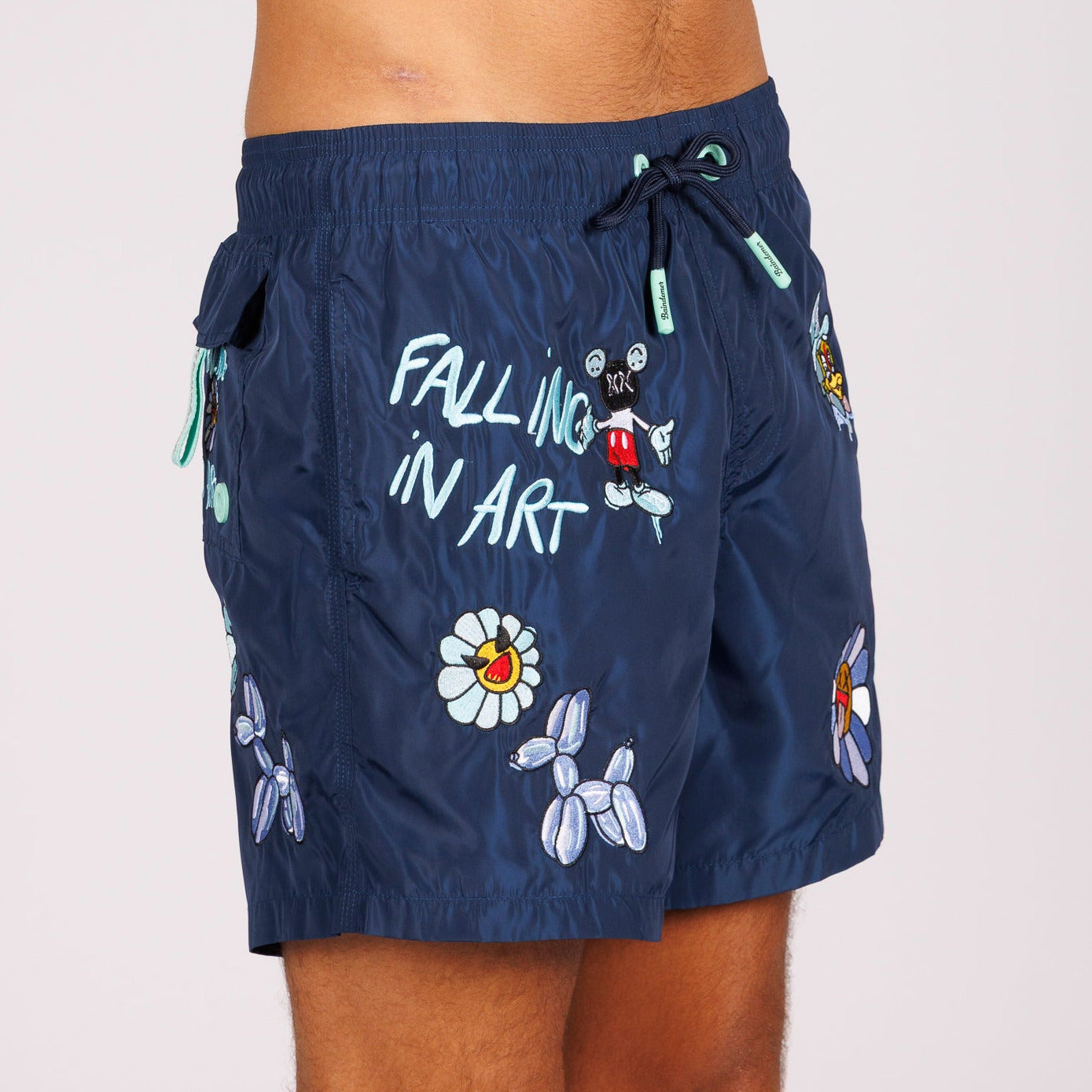 Navy blue swim shorts side view with illustrated graphic and “Falling in art” text