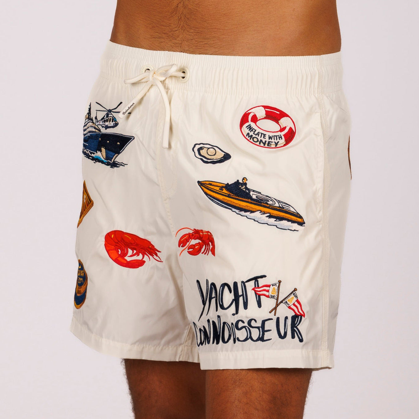 Off-white swim shorts side view with illustrated graphic and “Yacht connoisseur” text