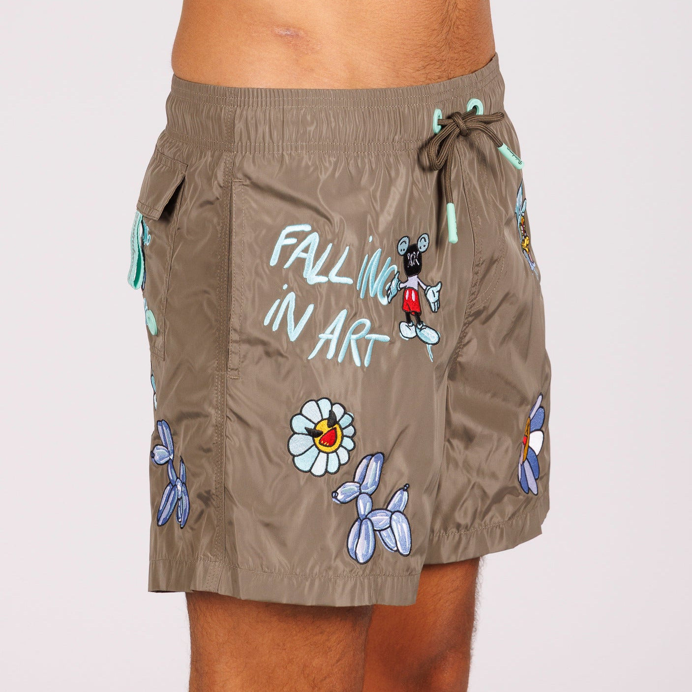 Khaki swim shorts side view with illustrated graphic and “Falling in art” text