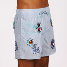 Light blue swim shorts side view with illustrated graphic and “Falling in art” text