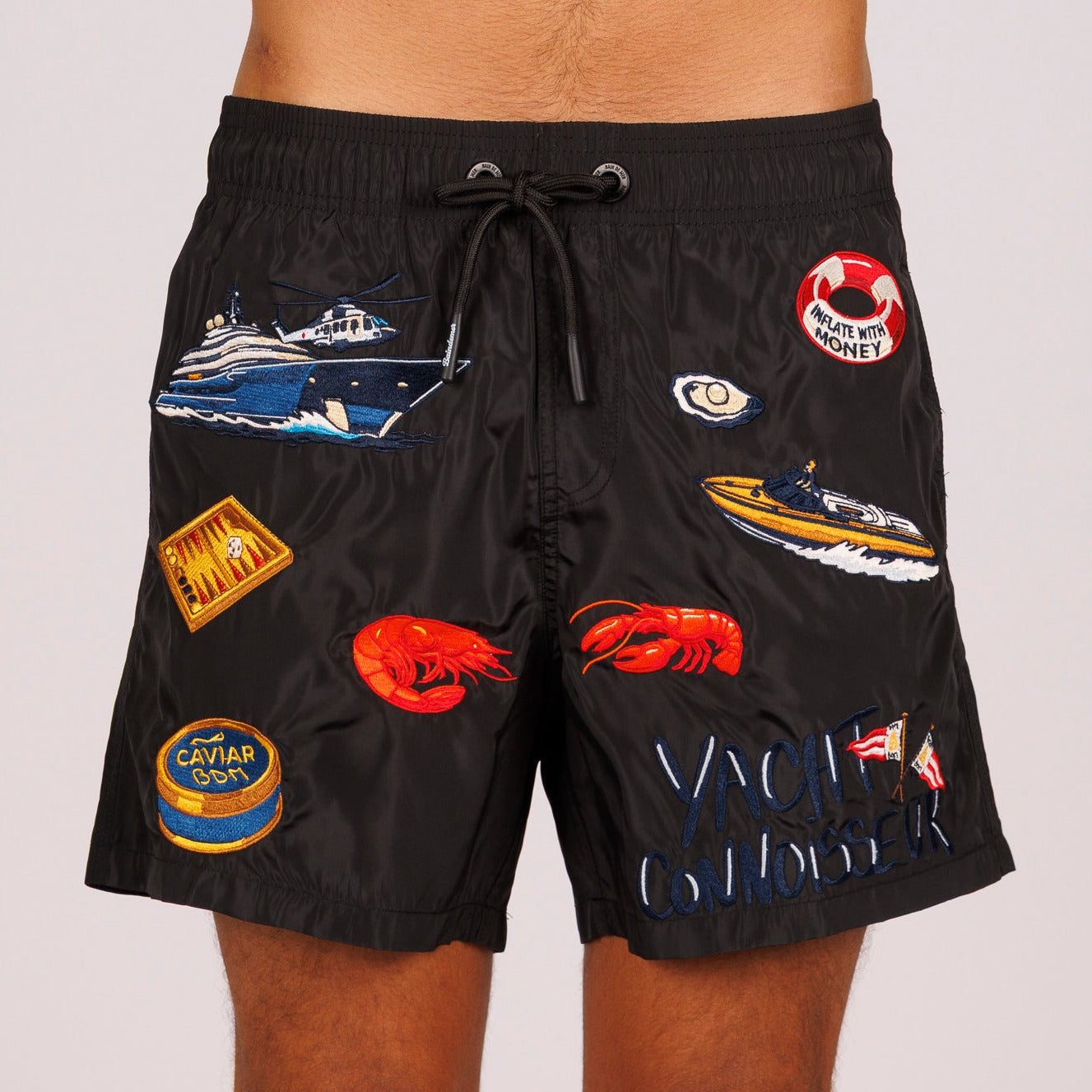 Black swim shorts front view with illustrated graphic and “Yacht connoisseur” text