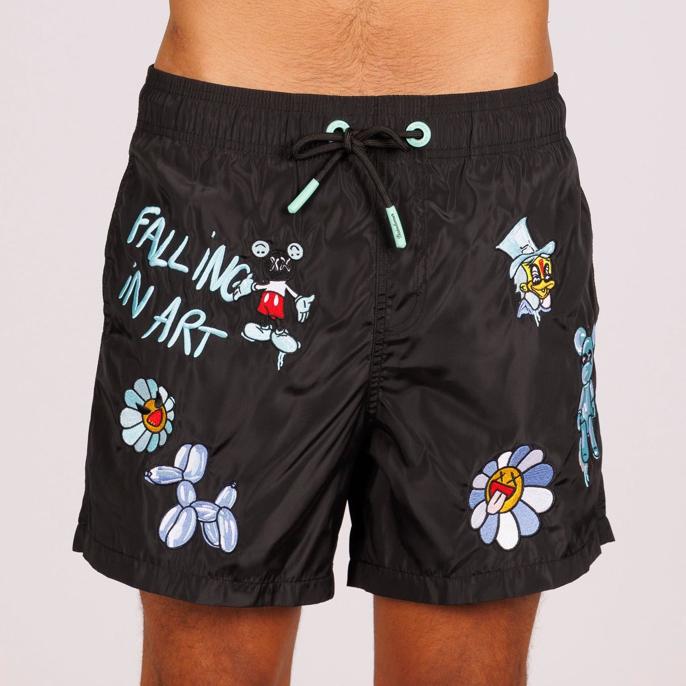 Black swim shorts front view with illustrated graphic and “Falling in art” text